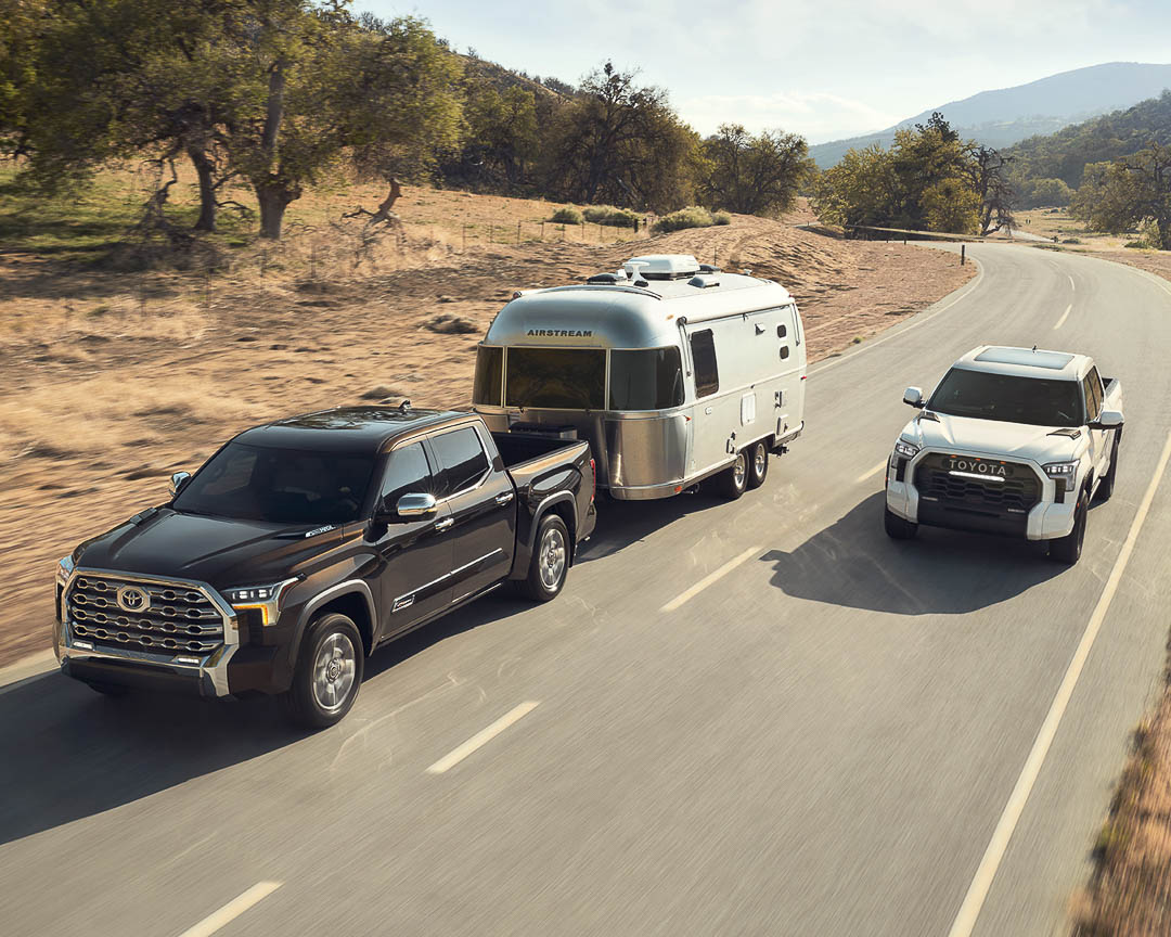 lateral front view of two 2022 Toyota Tundra on a road with one of them towing a travel trailer