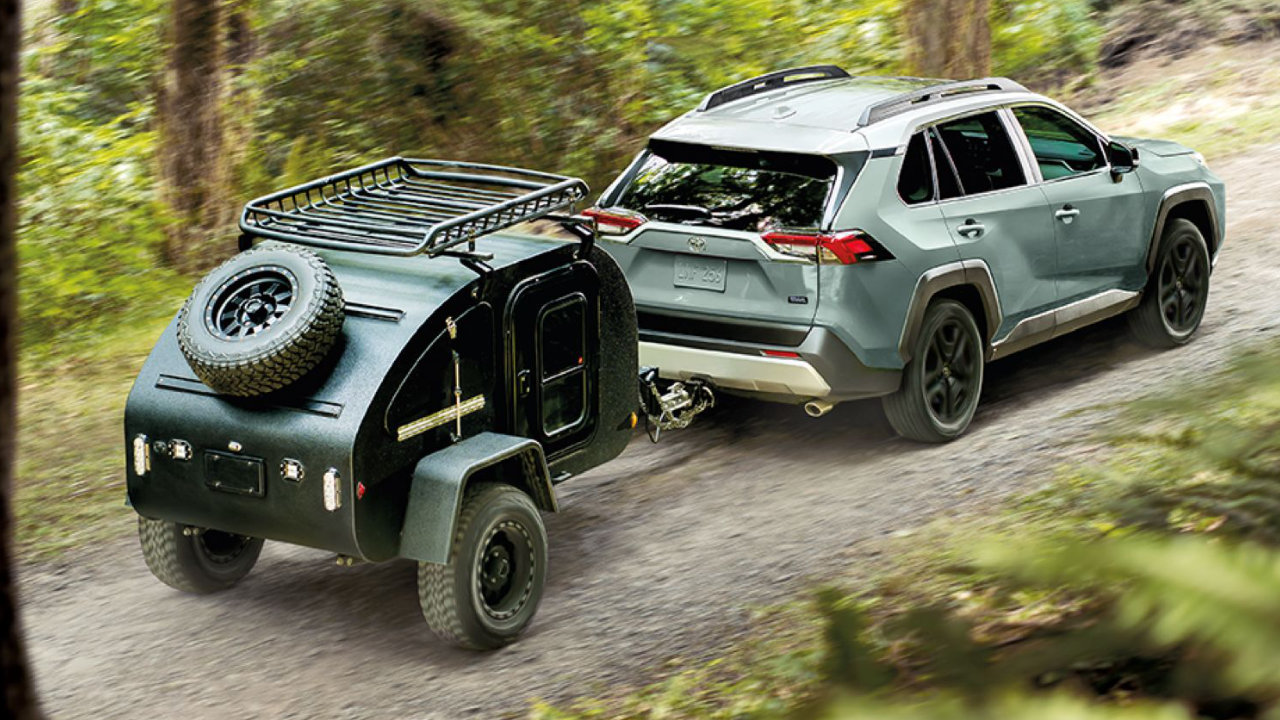 rear side view of a 2023 Toyota RAV4 hybrid carrying a trailer on a trail