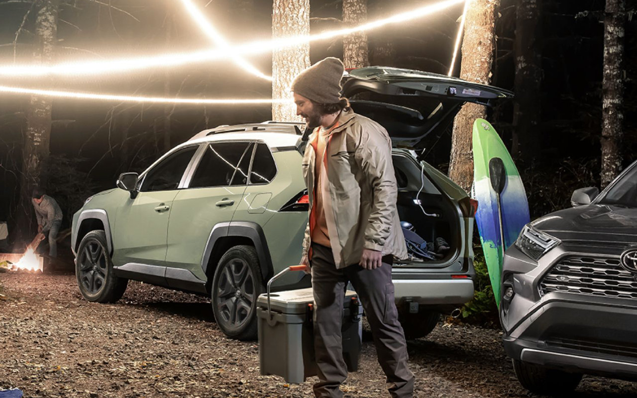 vue d'un campeur en train de décharger sa Toyota RAV4 2024 le soir, en forêt