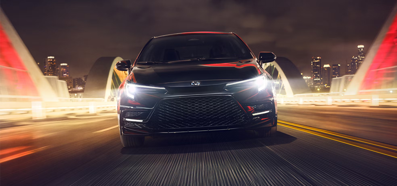 Vue avant du Toyota Corolla 2024 sur route en ville le soir, en pleine puissance