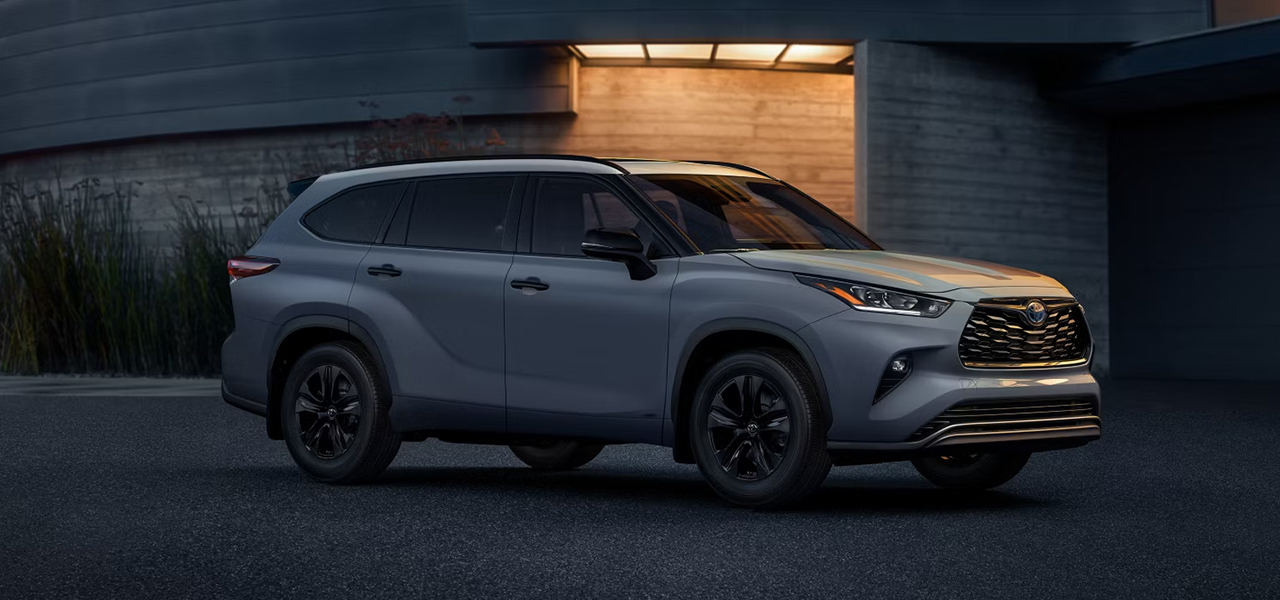 Vue 3/4 avant et latérale du Toyota Highlander 2024 garé le soir devant un bâtiment publique
